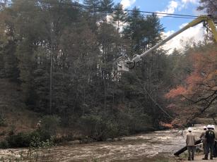 A Blue Ridge Mountain EMC crew pulls a tap line across the Toccoa River in Suches, Ga. at Cavender Gap and Highway 60. Lineman Chase Hemphill is in the bucket while crewmen Kelly Cruse, Clayton Wood, Jeff Odom, Terrence Kane, Chris Busbee, Jesse Miller and Josh Bryant wait to finish their duties after the tap line gets across the river.