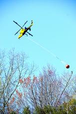 (Becky Long • Clay County Progress) A helicopter from the N.C. Forest Service in Franklin makes a run to retrieve water from a pond near the airport on Tusquittee Road Monday evening. The bucket can hold about 700 gallons of water and had to make multiple round trips.