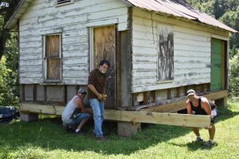 Woodhaven Construction owner Tommy Davis, center, was flanked by helpers Steve Johns, left and David Collins, right, to place the first piece of new lumber on the Old Hayesville Town Hall for the front porch.
