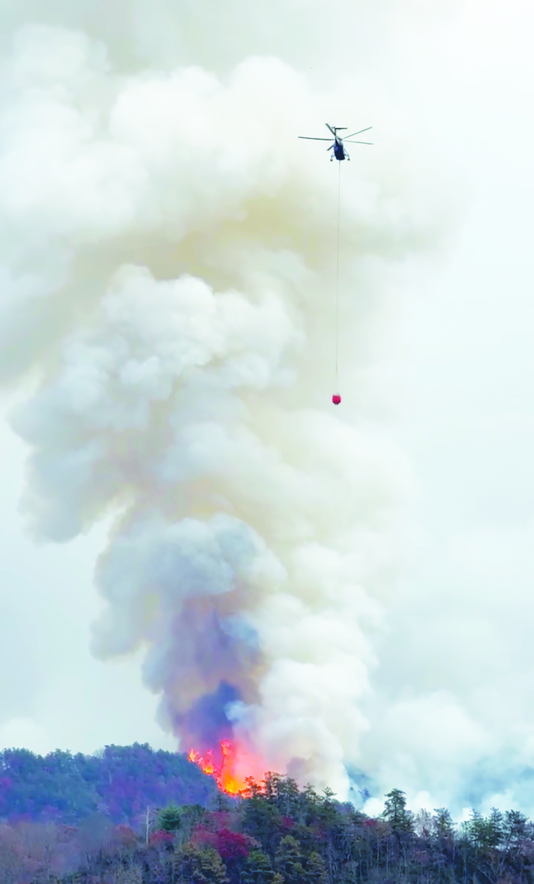 Photo by Randy Foster/editor@cherokeescout.com A heavy-lift helicopter prepares to drop water from a bucket on a hot spot in the Collett Ridge Fire east of Pisgah Road on Thursday.