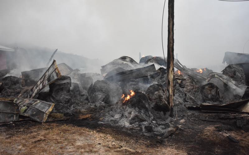 Hundreds of bales of hay smolder hours after the initial spark sent this hay barn up in flames.  (Progress photo by Travis Dockery)