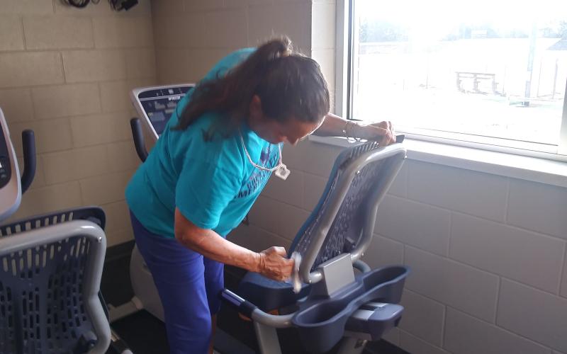 (Travis Dockery • Clay County Progress) Gym member Debra Bolle cleans a machine after her first workout since the reopening. Bolle was the first person to join the gym when it initially opened.