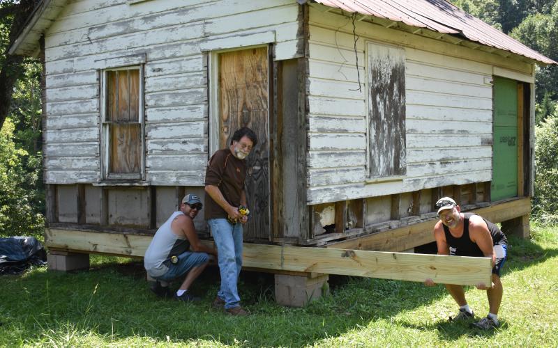 Woodhaven Construction owner Tommy Davis, center, was flanked by helpers Steve Johns, left and David Collins, right, to place the first piece of new lumber on the Old Hayesville Town Hall for the front porch.