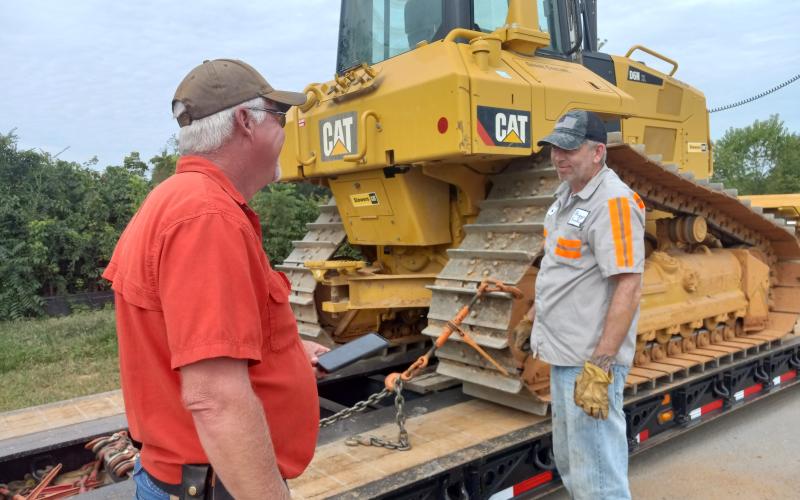 (Tracy Barnes/Staff Correspondent) Site supervisor Kelly Luther of Wells &amp; West Construction (left) talks with Travis Wilson, a driver for Biggs Transport. Wilson is loading out a GPS-equipped Cat Crawler Dozer, since grading is finished at the new school site in Peachtree.