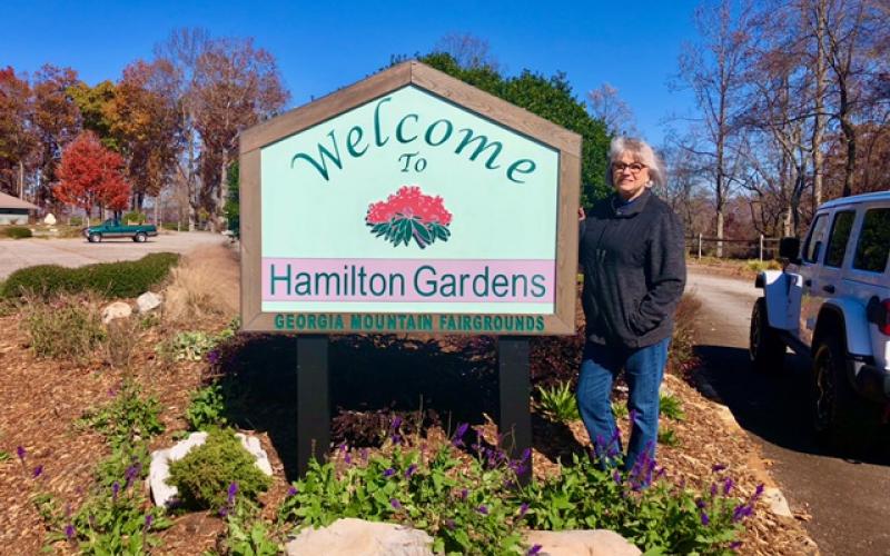 Margaret Windham stands beside the sign welcoming visitors.