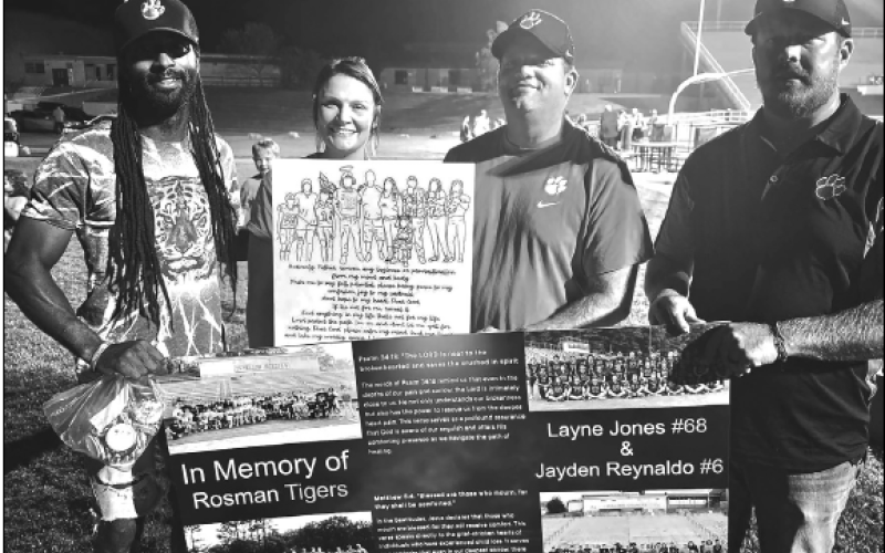 A large wall hanging THAT has been placed in the locker room of the Rosman Tigers was presented by Miranda Shuler during a memorial for Layne Jones and Jayden Reynaldo. With Miranda during the presentation are Rosman coaches, Tyrea Allen, Courtney Cheek and Chris Owen.