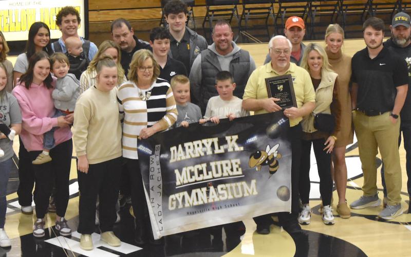Gary Corsair • Clay County Progress Coach Darryl McClure holds helps hold the banner naming the gymnasium in his honor for a stellar career as girls’ high school basketball coach. He is surrounded by family members including his wife, Linda (helping hold the banner).