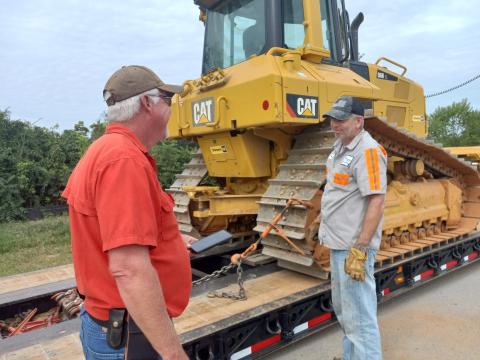 (Tracy Barnes/Staff Correspondent) Site supervisor Kelly Luther of Wells & West Construction (left) talks with Travis Wilson, a driver for Biggs Transport. Wilson is loading out a GPS-equipped Cat Crawler Dozer, since grading is finished at the new school site in Peachtree.