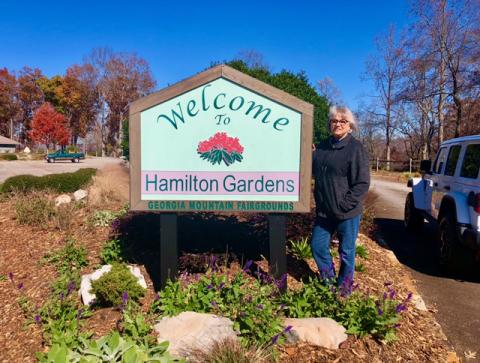 Margaret Windham stands beside the sign welcoming visitors.