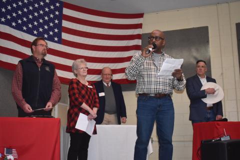 Becky Long • Clay County Progress Fort Hembree Pastor Harold Holbrook Jr., center, opens Saturday’s debate with prayer. He is joined on stage by, from left, U.S. Rep. Chuck Edwards, Clay County Republican Chairperson Barbara Deas, moderator Larry Ford and congressional primary candidate Christian Reagan. The venue for the debate was Brasstown Community Center which holds about 165 people and was filled to near capacity.