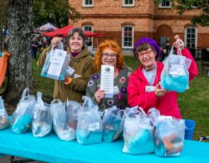 Photo • Ron Wallace HHI Volunteers, from left,  Misti Muscat, Lynne Maniotes and Wendy Slaton hold up gift bags for attendees to use as they enjoy wine, beer, food or items from crafty vendors during the annual Steins & Wine event. 
