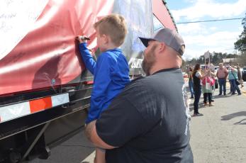 Abigail Blythe Batton • Cherokee Scout  Colt Allen, 6, of Hayesville, gets a boost from his dad, Dwayne Allen, to sign his name to the U.S. Capitol Christmas Tree truck Sunday in Murphy.