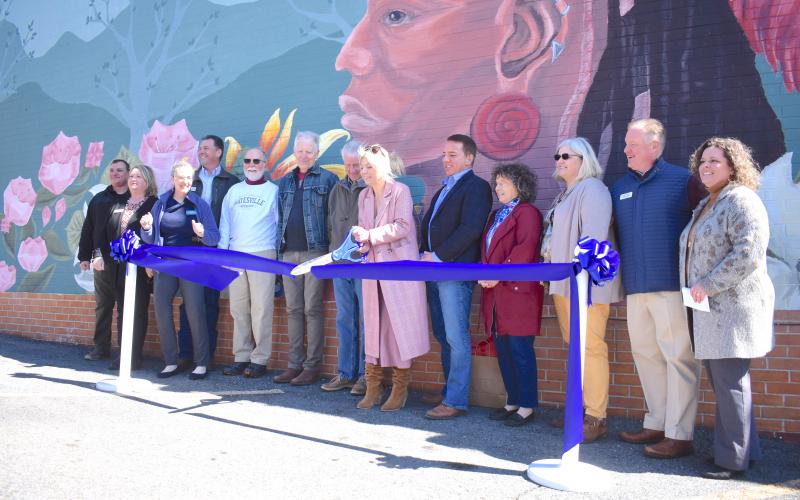 Artist Corrina Luckenbach, flanked by Eastern Band of Cherokee Indians Chief Richard Sneed and representatives from multiple organizations, cuts the ribbon on her work. The original mural was painted in 1992 by then Boy Scout Matthew Smith. Smith’s father Stephen was in attendance of the ribbon cutting which was held on Tuesday, April 19.