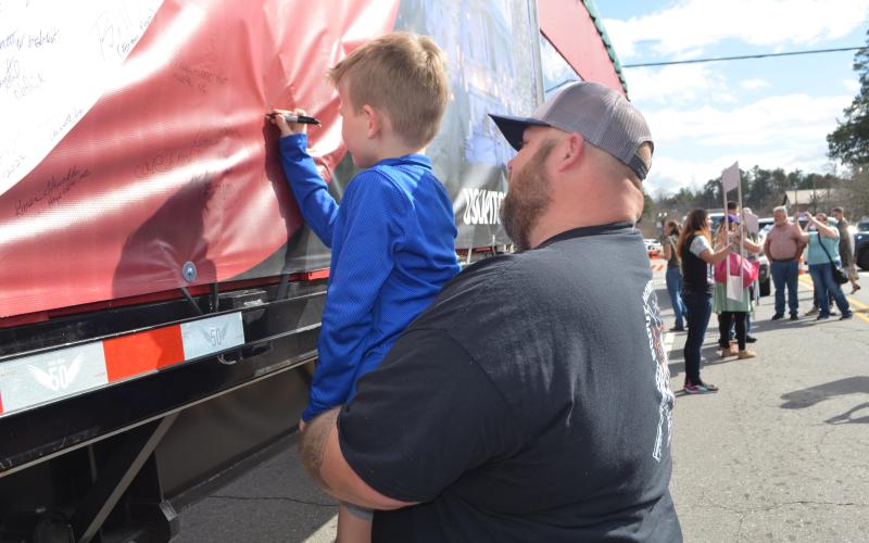 Abigail Blythe Batton • Cherokee Scout  Colt Allen, 6, of Hayesville, gets a boost from his dad, Dwayne Allen, to sign his name to the U.S. Capitol Christmas Tree truck Sunday in Murphy.