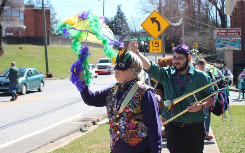 Megan Broome/The Clayton Tribune. Teri Dobbs goes all-out and dances in the One Man Band parade for the second annual Mardi Gras sponsored by the Rabun County Chamber of Commerce on Saturday, Feb. 22. Kaleb Wilburn plays the trombone as the group travels through downtown Clayton.